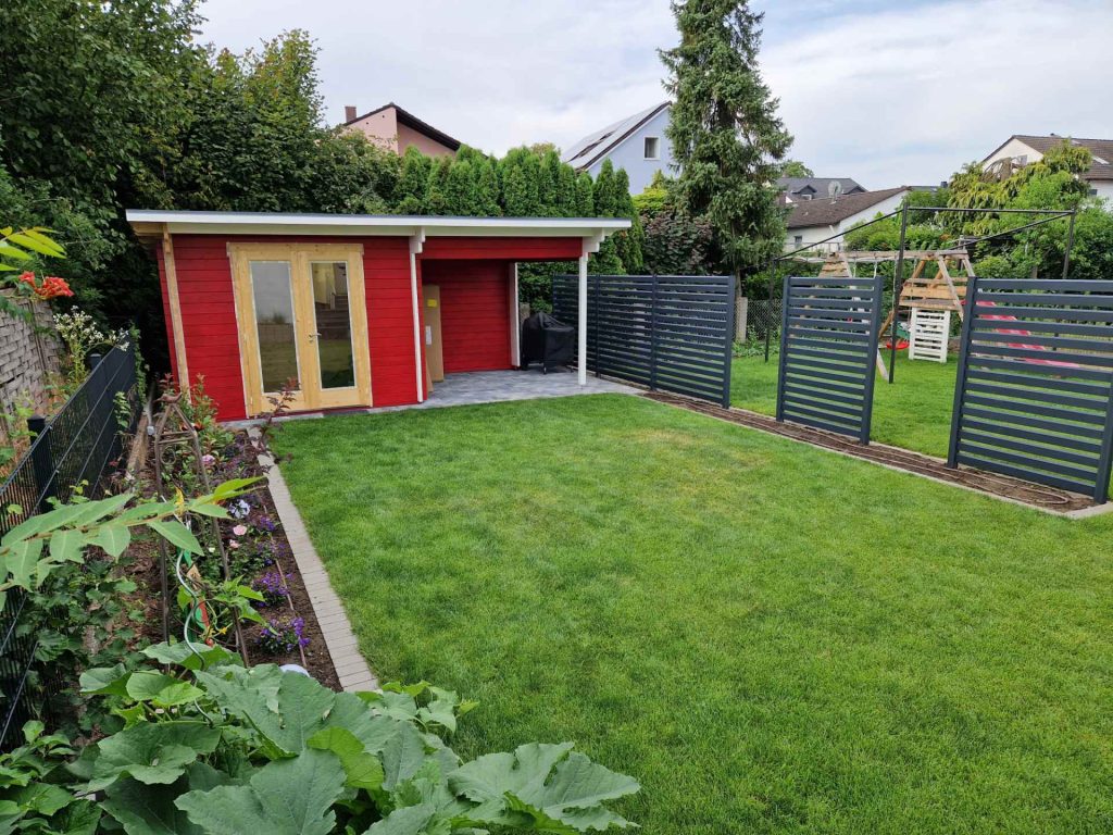 Rotes Gartenhaus, Rasen, Spielplatz und Beet mit Pflanzen, Schaffrin Garten und Landschaftsbau